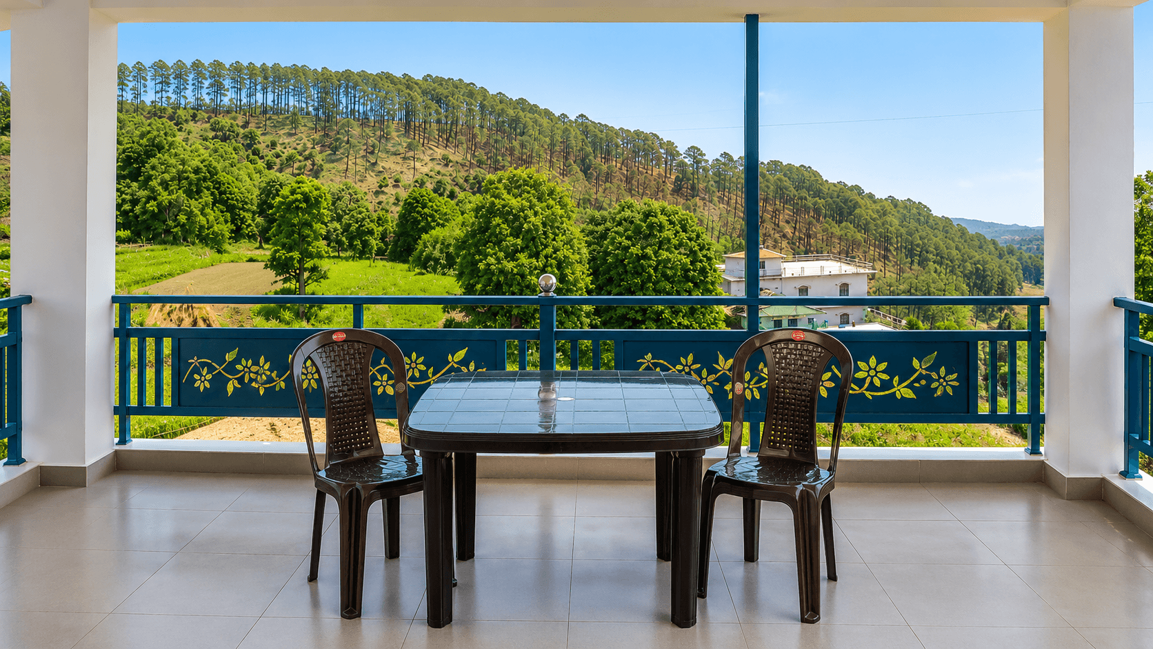 Balcony table and chairs facing pine-covered hills at Himgiri Home Stay